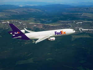 FedEx Frachtflugzeug fliegt über schneebedeckte Berge und grüne Täler. — Fedex Hintergrundbild