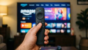 Mano sosteniendo el control remoto Amazon Fire TV con interfaz de streaming en el fondo.