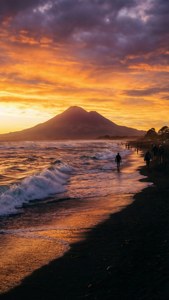 Matahari terbenam yang cerah di Pantai Fitzroy dengan latar belakang Gunung Taranaki