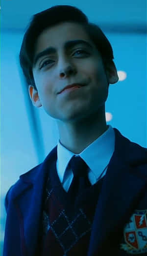 A young boy in school uniform smiling softly in blue light.