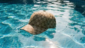 Surreal image of Gucci hat floating in pool water with sunlight and ripples.