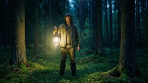Potret senja misterius Jakob Züberlein dengan lentera di hutan gelap.