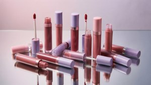 Flatlay elegante de tubos de gloss em uma superfície espelhada com tons pastéis, ideal para entusiastas de maquiagem.
