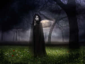 Eine mysteriöse Frau in einem dunklen Umhang steht in einem nebligen, mondbeschienenen Wald bei Nacht. — Gothic Fantasy Wallpaper