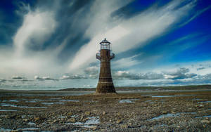 A wooden lighthouse on a rocky shore under a stormy sky. — Lighthouse Background