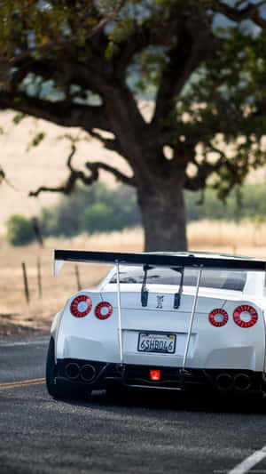 White Nissan GT-R sports car parked on a country road under a large tree at sunset. — Car iPhone Picture