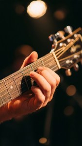 Lähikuva kitaran kielestä, jota näppäillään bokeh-valojen kanssa, musiikkitaustakuva