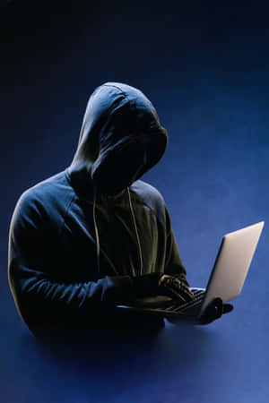 Anonymous hooded person typing on laptop in dim blue light. — Hacker Wallpaper