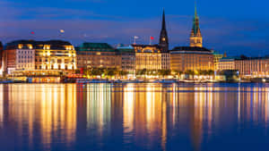Hamburgs bysilhuet ved skumring med glødende bygninger reflekteret i floden.