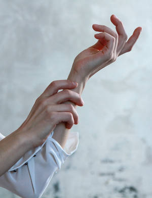 Les mains d'une personne touchant doucement son poignet contre un mur blanc texturé.