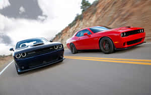 Two Dodge Challengers racing on a mountain road with motion blur.