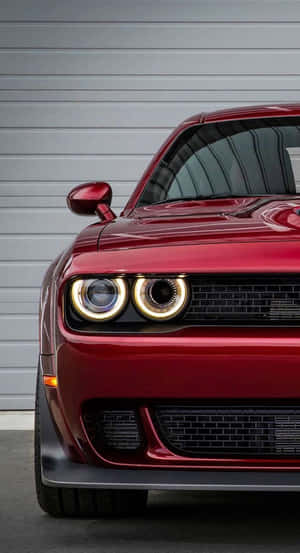 Nahaufnahme der Front eines roten Muscle-Cars mit leuchtenden Scheinwerfern. — Hellcat iPhone Wallpaper