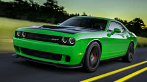 Um Dodge Challenger SRT verde acelerando em uma estrada com linhas amarelas e árvores desfocadas ao pôr do sol. — Hellcat Papéis de Parede
