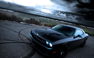 Black muscle car parked on coastal road during stormy dusk.