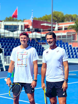 Two male tennis players smiling on a blue hard court with empty stadium seats in background. — Holger Rune Picture