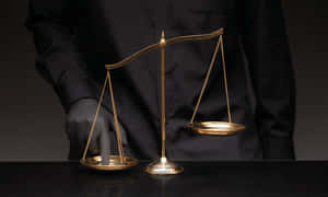 Main en gant noir ajustant une balance dorée de la justice sur table sombre.