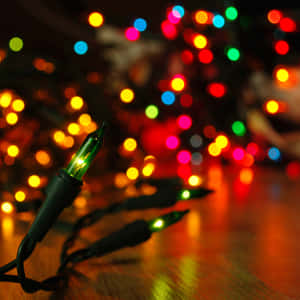 Nahaufnahme einer glühenden grünen Lichterkette mit bunten Bokeh-Lichtern im Hintergrund.