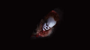 A scary clown with red hair and white makeup stares from darkness. — It 2017 Picture
