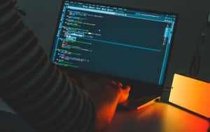 Person coding on laptop under warm orange light at night. — It Computer Picture
