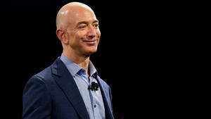 Jeff Bezos in einem blauen Anzug, lächelnd vor einem schwarzen Hintergrund.