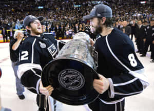 Two hockey players celebrate with the Stanley Cup on ice in front of fans.