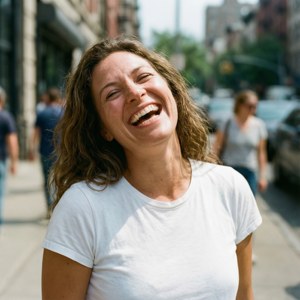 A woman laughs joyfully on a sunny city sidewalk. — Grace fulton Picture