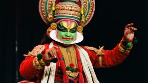 Seorang penari Kathakali yang dramatis dengan riasan dan kostum tradisional di bawah lampu panggung.