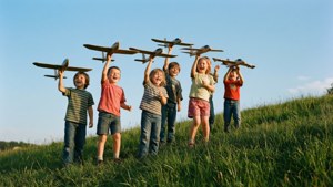 Kinderen spelen met modelvliegtuigen op een zonnige heuvel.