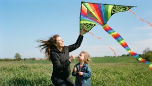 Una mamma autistica e un bambino fanno volare un aquilone in un campo erboso sotto un cielo blu.