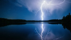 A lightning bolt reflected in a calm lake at night.
