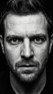 Potret hitam putih kontras tinggi Richard Archer dengan ekspresi intens.
