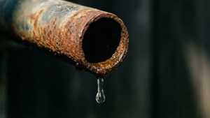 Et nærbillede af et rustent rør, der drypper vand, som symboliserer spild og hast.