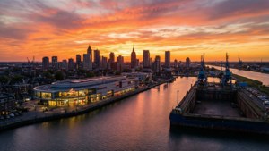 City skyline at sunset with orange clouds reflected in water beside a modern building and dockyard. — Lelystad Picture