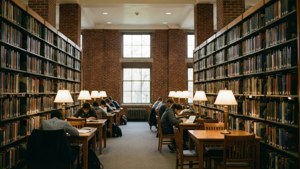 Interiør av UofL-biblioteket med bokhyller og studenter som studerer i varmt lys