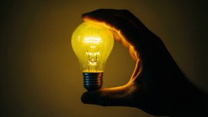 Mano che tiene una lampadina gialla luminosa in silhouette su sfondo scuro