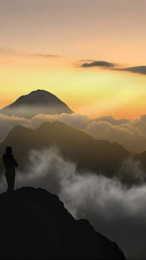 Person standing on mountain peak watching sunrise over clouds and distant volcano. — Sun PNG