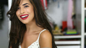 Una mujer sonriente con cabello oscuro y labial rojo que lleva una blusa blanca en interiores. — Mac Cosmetics Fondos de pantalla