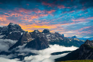 Snowy mountain peaks rise above clouds at sunset with colorful sky — Macbook Wallpaper