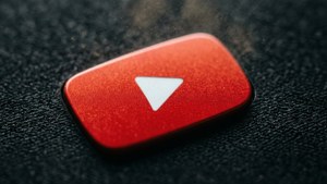 Close-up makro dari tombol putar YouTube merah pada permukaan hitam bertekstur dengan partikel debu.