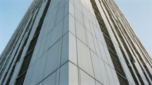 Eine moderne Architekturaufnahme eines schlanken Wolkenkratzers, verkleidet mit matten hellgrauen Magnesiumlegierungspaneelen.