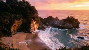 Coastal cliff with waterfall and ocean waves at sunset — macOS Big Sur Wallpaper