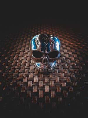 Anel de caveira metálico brilhante sobre uma esteira escura tecida com iluminação dramática. — Skull Papéis de Parede