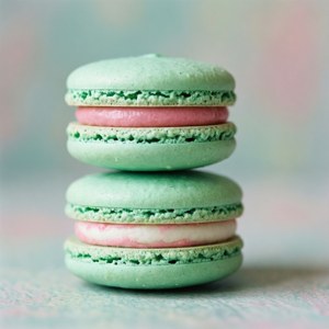 Stack of mint green macarons with pink and white on pastel background.