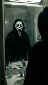 Ghostface verschijnt in een badkamerspiegelreflectie, wat een gespannen horror-sfeer creëert.