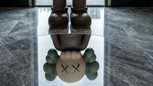 Kaws BFF seisoo heijastavalla harmaalla lattialla luoden peilikuvan.