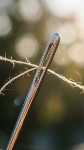 Foto makro mata jarum dengan benang, bokeh, dan cahaya hangat.