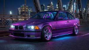 BMW E36 coupé roxa com iluminação inferior em uma ponte à noite.