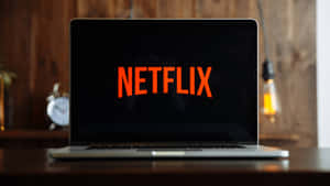 Laptop showing Netflix logo on wooden desk with warm lighting and clock. — Netflix Wallpaper