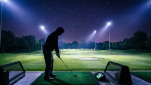 En stemningsfuld natscene på en driving range med en ensom golfspiller under skarpe projektørlys.