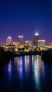 City lights reflect on a river under a starry night sky.